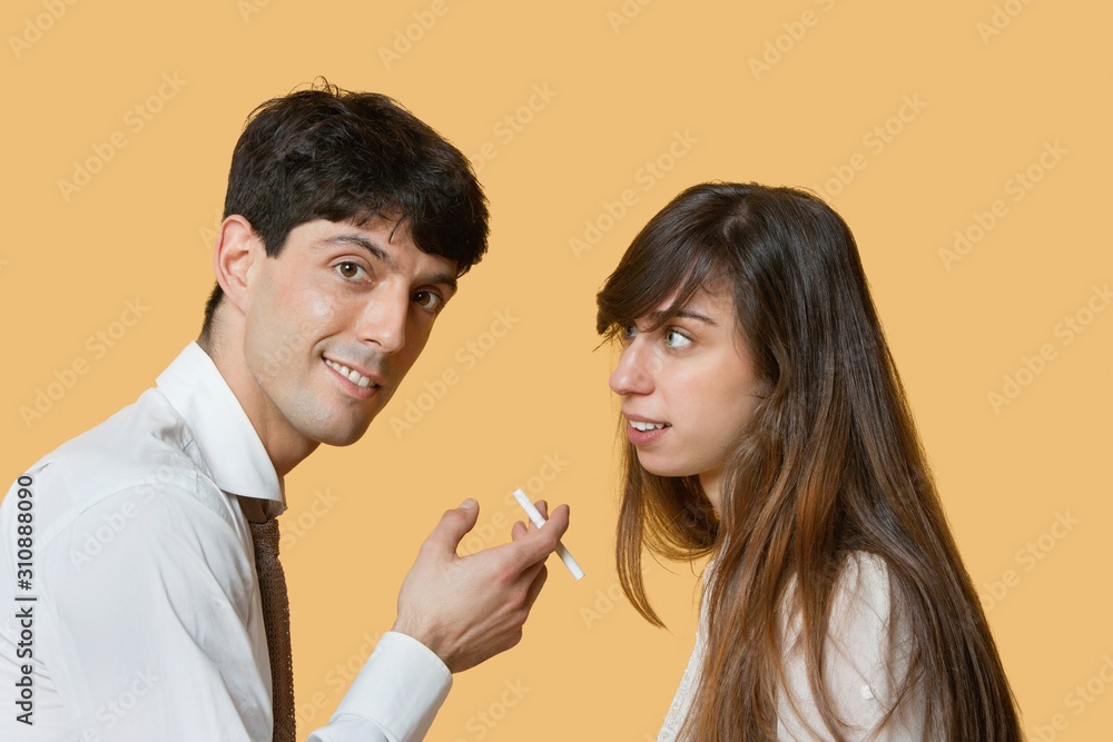 Portrait of a young man with cigarette while woman looking at him over colored background Portrait of a young man with cigarette while woman looking at him over colored background