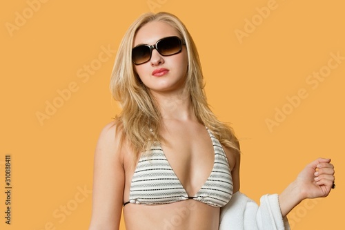 Beautiful young woman in bikini with towel in hand over colored background