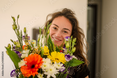 Beautiful young brunette girl with brown eyes holds a bouquet of flowers in her hands and smiles on International Women's Day or Valentine's Day. Lifestyle, natural natural beauty, without retouching