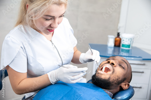 Young african-american man visiting dentist's office for prevention and treatment of the oral cavity. Man and woman doctor while checkup teeth. Healthy lifestyle, healthcare and medicine concept.