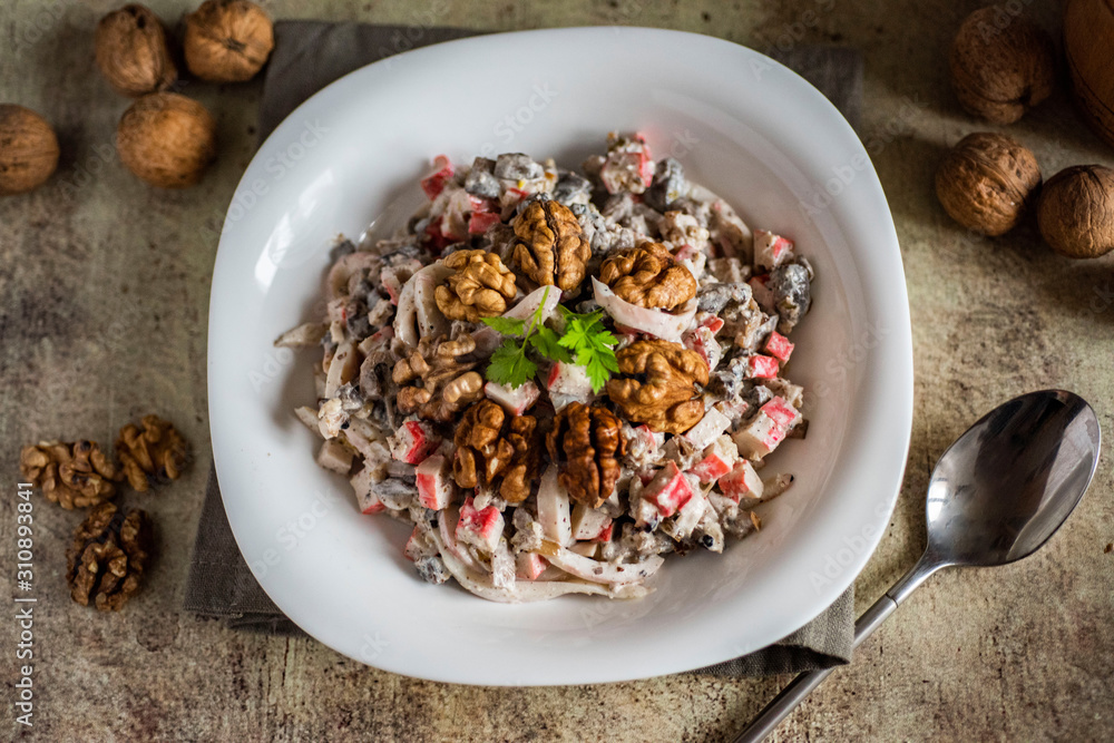 Delicious salad with squid and walnuts. Seafood salad in a white plate on a gray background Delicious salad with squid and walnuts. Seafood salad in a white plate on a gray background