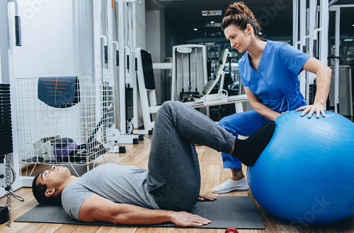 Physiotherapist helping doing exercises a man, a former military man, treatment of injuries in a military hospital. photo