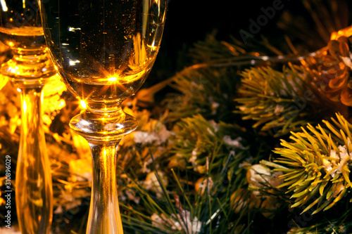 Two glasses of champagne with fir branches and garland light. New year greeting card. Selective focus.