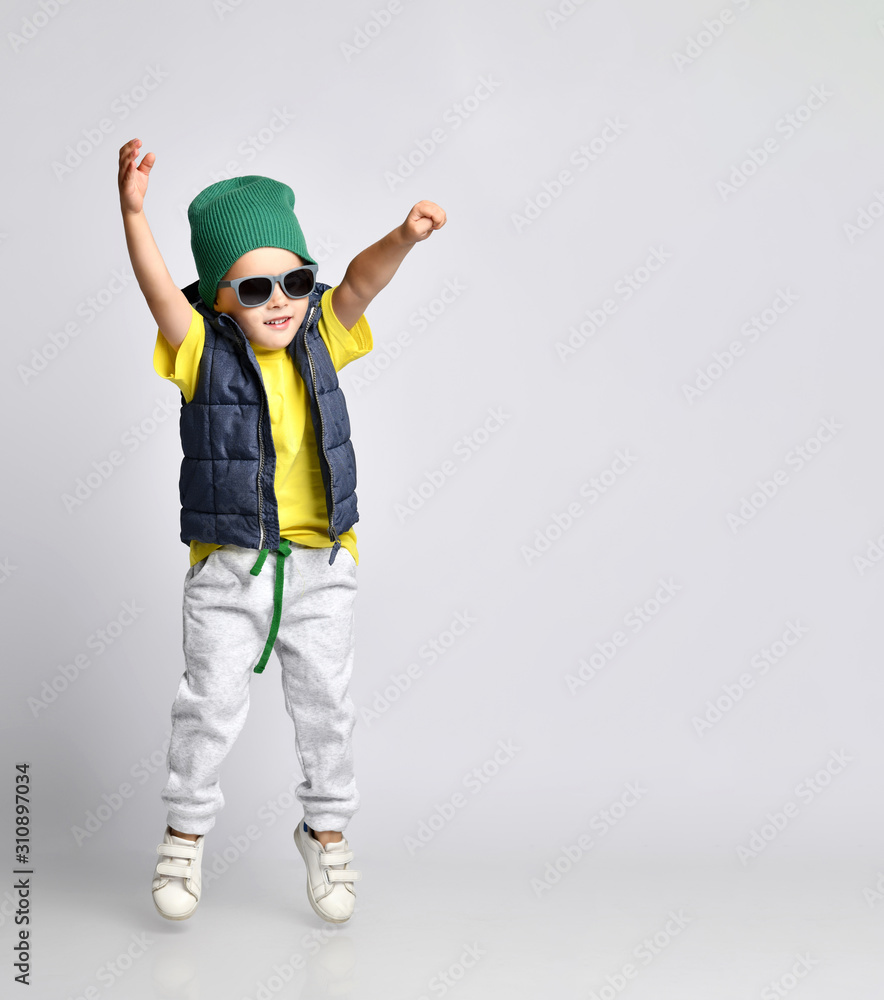 Stylish cheerful little boy 4 years old in sweatpants, a green hat, glasses and a down vest has fun Stylish cheerful little boy 4 years old in sweatpants, a green hat, glasses and a down vest has fun