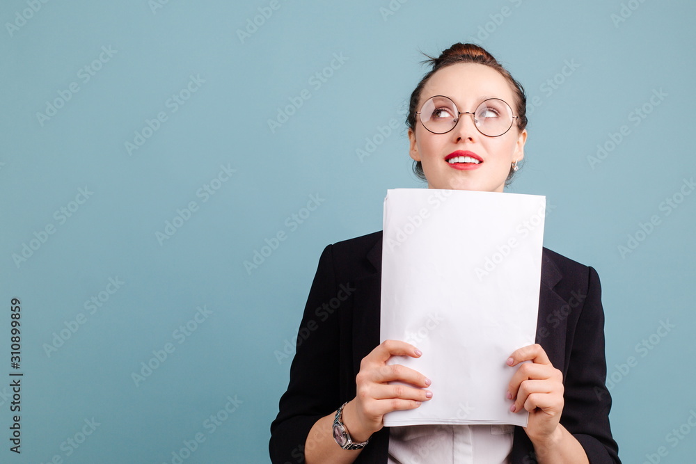 Pensive girl in glasses and office suit looking at the ceiling holding blank sheets of white paper Pensive girl in glasses and office suit looking at the ceiling holding blank sheets of white paper