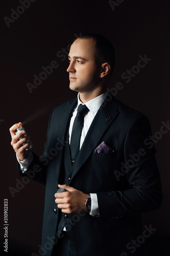 Man applies perfume and smells fragrance. Handsome guy is choosing perfumes, Elegant man in suit using cologne,groom getting ready in the morning before wedding ceremony