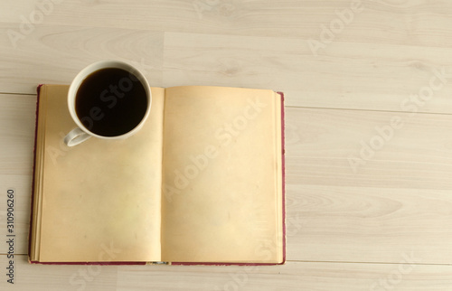 a cup of coffee and an open book on white wooden background.Top view,space for text.