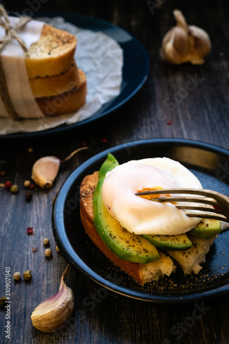 Avocado poached egg on a golden crouton with garlic and pepper. In the background are the loafs of waxed paper. Vegan Healthy Eating.