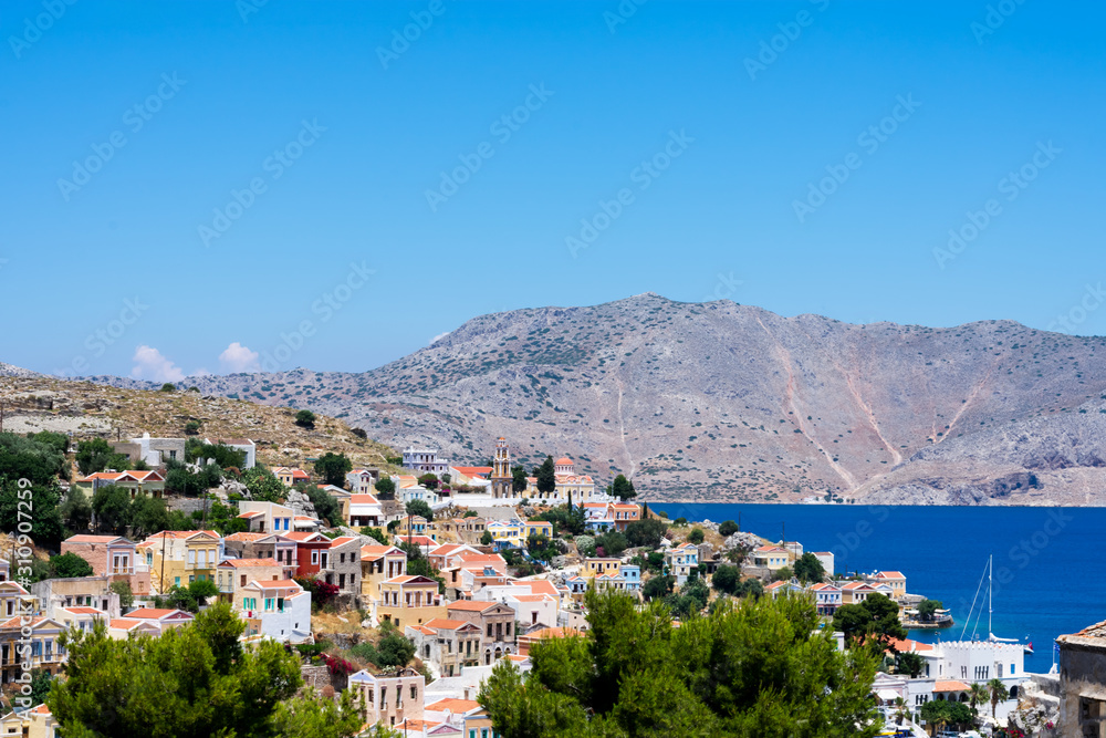 Amazing view on tiny colorful houses on rocks and oleander trees near the Mediterranian sea on Greek island in sunny summer day, vacation on exotic islands