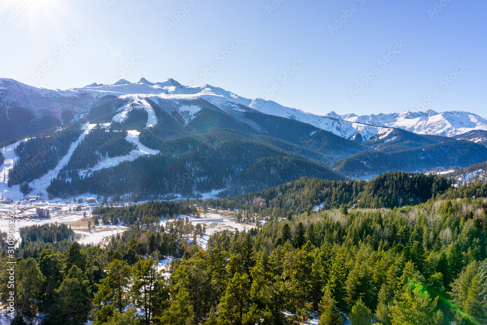 Obraz premium Winter sunny landscape with snowy peaks of mountain ranges with green trees and blue sky