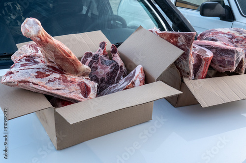 Cardboard boxes with frozen pieces of meat are on the hood of the car.