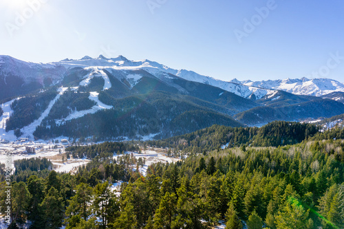 Winter sunny landscape with snowy peaks of mountain ranges with green trees and blue sky © vika33
