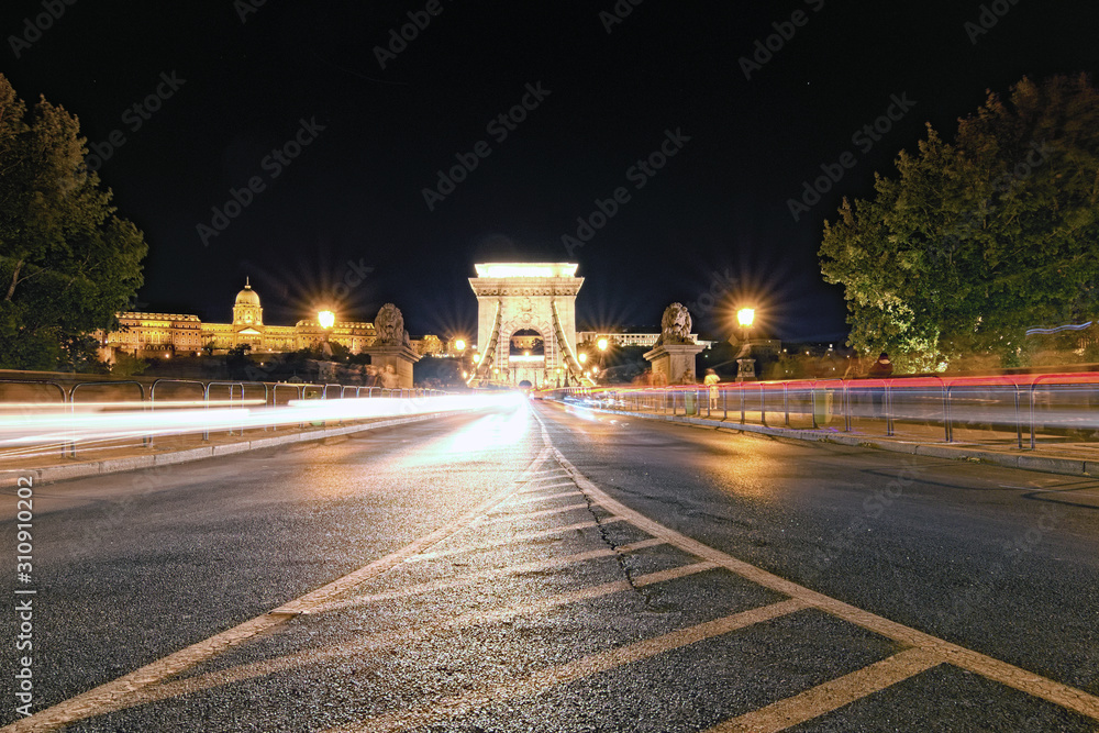 Low perspective view of illuminated Chain Bridge. The Buda Castle (Royal Palace) in the background. Colorful light trails with motion blur effect, long time exposure. Budapest, Hungary
