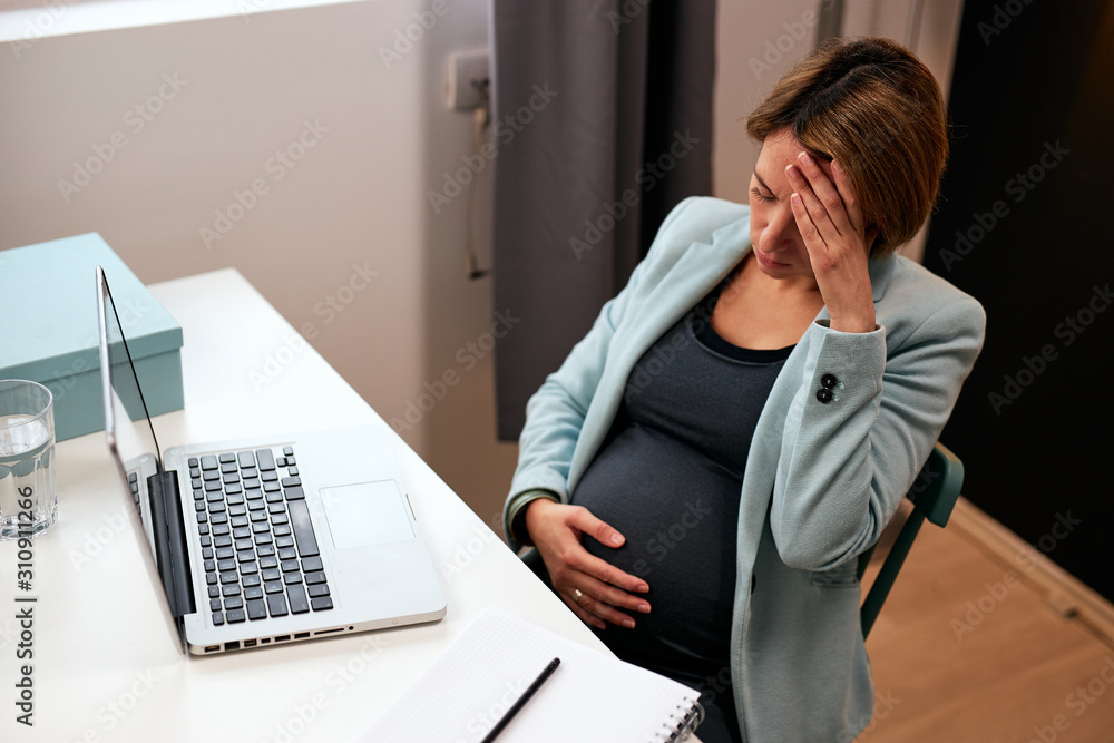 Pregnant businesswoman in forties sitting in her office, touching belly and having headache. Pregnant businesswoman in forties sitting in her office, touching belly and having headache.