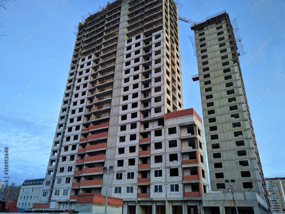 Construction of a multi-storey monolithic house of gray concrete against the blue sky