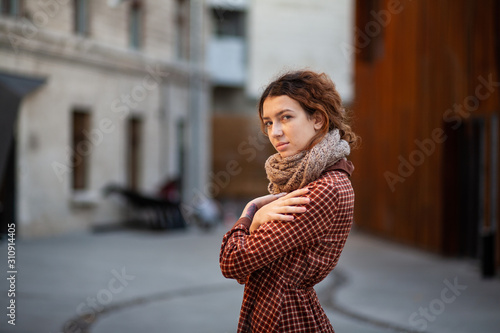 Dreaming young woman with spectacular curly red ginger hair looking at camera posing outdoor in downtown street. Female portrait.