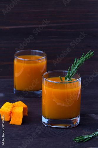 detox cocktail. two glasses of fresh juice of pumpkin with sprig of rosemary, slices of ripe pumpkin on dark wooden background. vertical orientation.