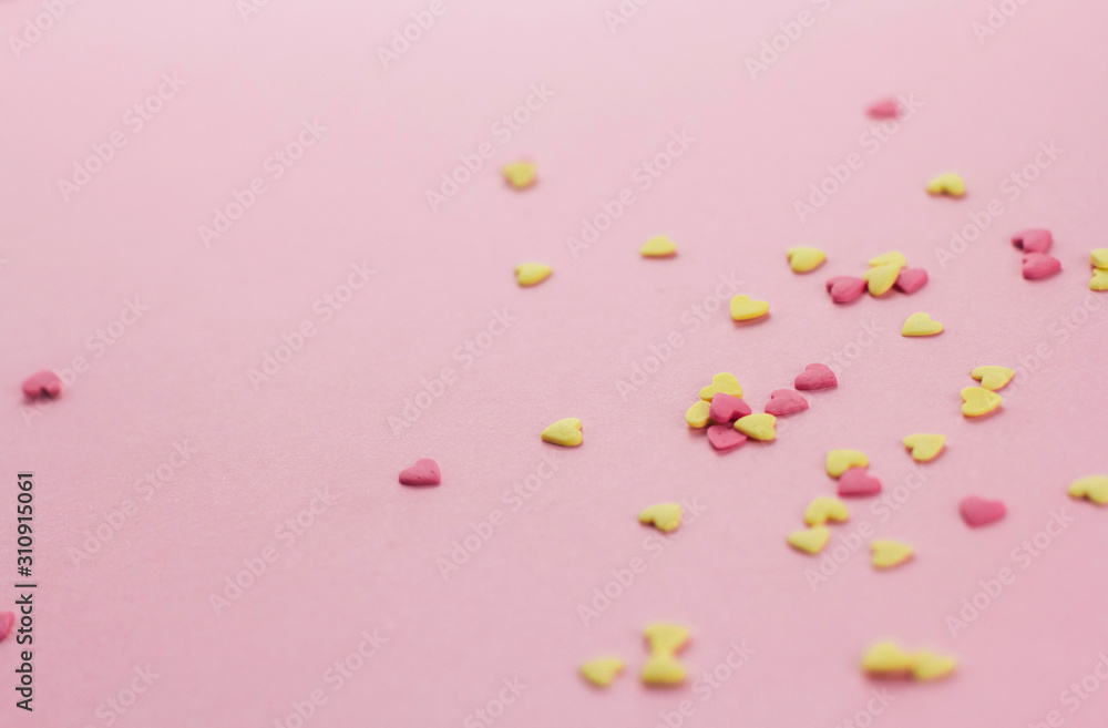  falling yellow and pink heart-shaped confectionery confetti on a pink background copy space.
