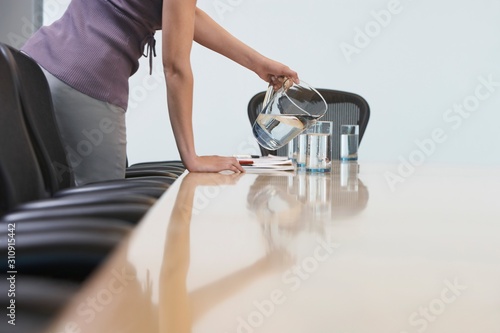 Midsection Of Female Worker Pouring Water Into Glasses On Conference Table