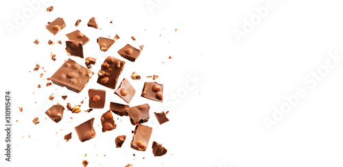 Flying in the air broken bar of milk chocolate with nuts and flakes isolated on white background. Chocolate pieces levitation concept.