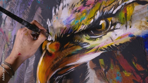 Artist designer draws an eagle on the wall. Craftsman decorator paints a picture with acrylic oil color brush. Close-up dark magic cinematic look. Painter dressed in a paint coat. Indoor.