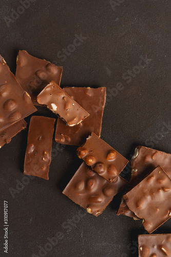 The chunks of broken different chocolate bars with nuts on the black stone surface with space for text. Background with chocolate. Sweet food photo concept.