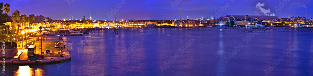 Panoramic view at blue hour on the Old Town of Taranto, Puglia, Italy, and in the background the highly polluting steel plant, former Ilva, now ArcelorMittal