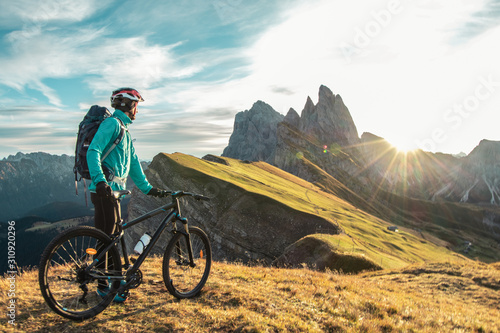 Young man with mountain bike on Seceda mountain peak at sunrise. Puez Odle, Trentino, Dolomites, Italy. photo