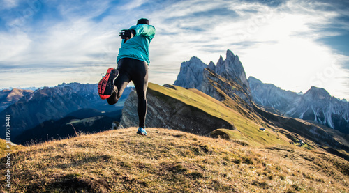 Young man in sport trail clothes running on Seceda mountain peak at sunrise. Puez Odle, Trentino, Dolomites, Italy.