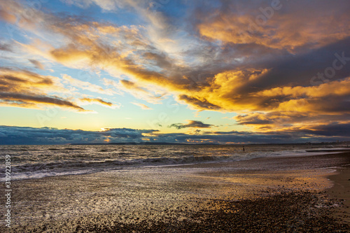 A view of a stony beach at sunset with crashing waves and ecume under a majestic yellow cloudy stormy sky