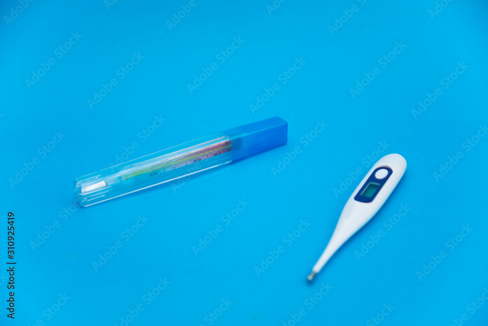 The medical mercury thermometer in plastic case and electronic thermometer lie over light blue background. Medical care. Selective focus. Flat view The medical mercury thermometer in plastic case and electronic thermometer lie over light blue background. Medical care. Selective focus. Flat view
