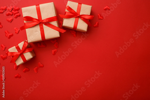 Presents with red bow on red background with heart confetti. Flat lay style. Valentine day concept