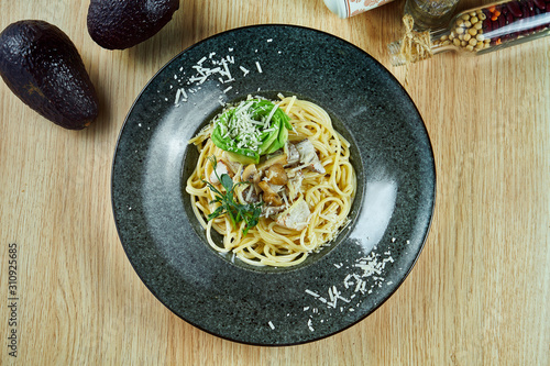 Appetizing pasta with porcini mushrooms, avocado and parmesan in a black plate on a wooden background. Italian cuisine. Top view flat lay food.