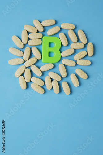 Vitamin B in pills with the letter B on a blue background. Flat lay. Top view. Copy space. Vertical photo.