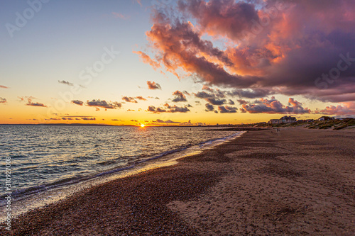 A view of a stony beach at sunset with crashing waves and ecume under a majestic yellow cloudy stormy sky photo