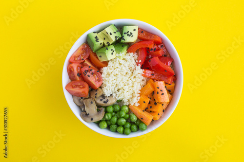 Vegan poke bowl with couscous and vegetables in the white bowl in the center of the yellow background. Top view. Copy space. Closeup.