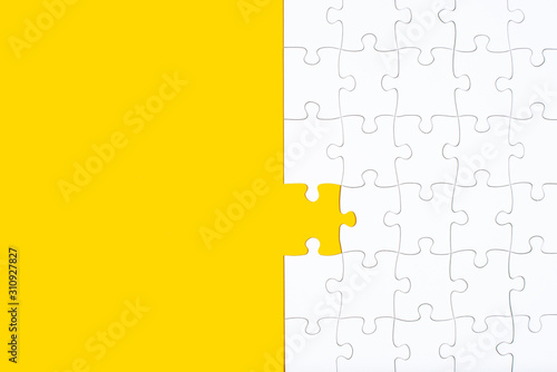 Unfinished white jigsaw puzzle pieces on yellow background photo