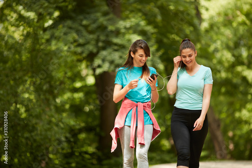 Two beautiful caucasian fit girlfriends in sportswear walking in nature and listening music.
