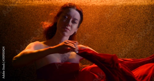 a cute girl with long hair moves her hands beautifully with a red cloth in a stream of bubbles under the water. contour bright orange light. close up