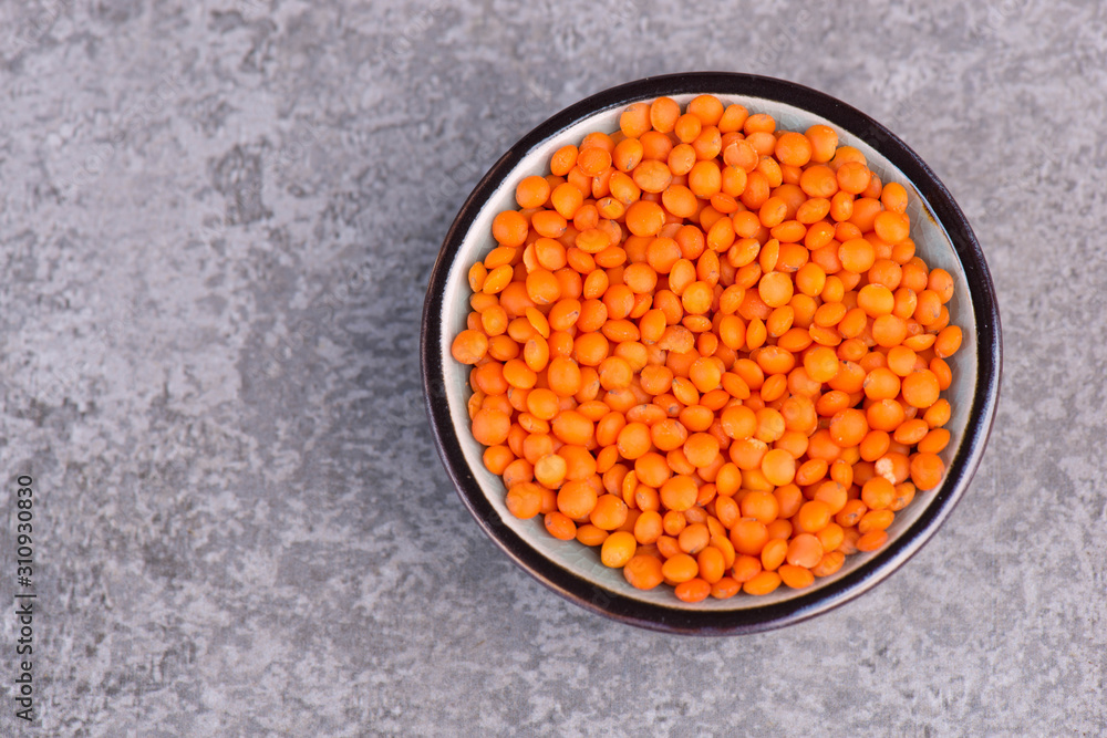 Red lentils in a bowl on a grey structured background Red lentils in a bowl on a grey structured background