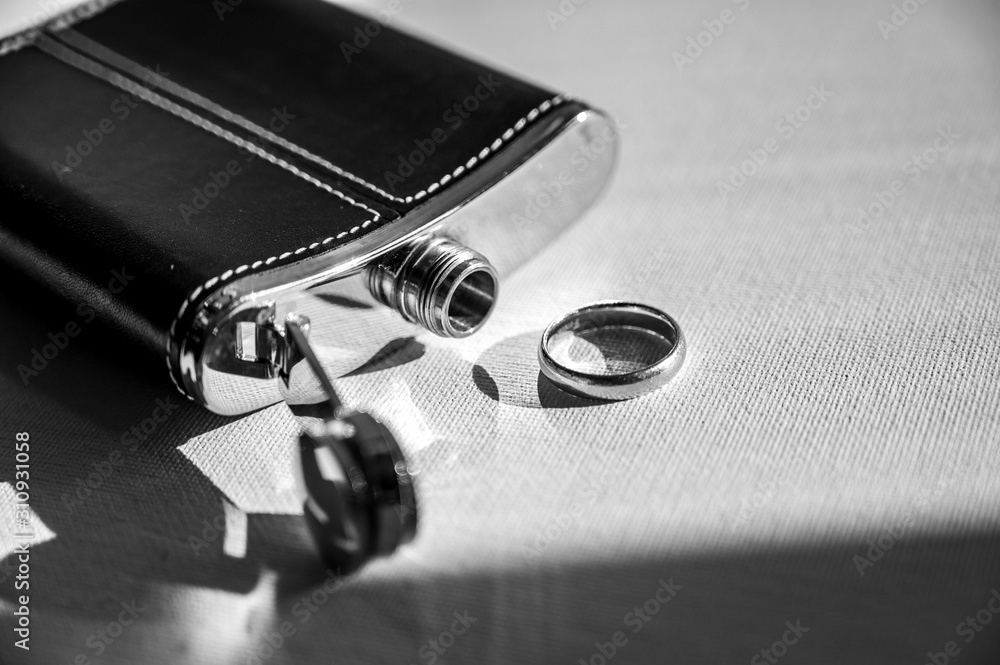 Black and silver whiskey flask and a wedding ring Black and silver whiskey flask and a wedding ring