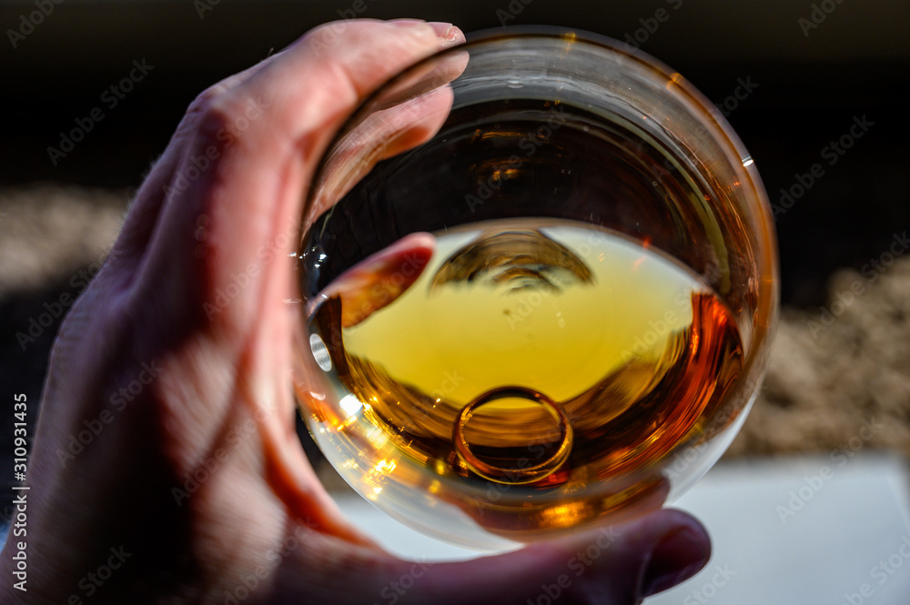 Caucasian hand holding a glass of amber colored liquid with a wedding ring at the bottom