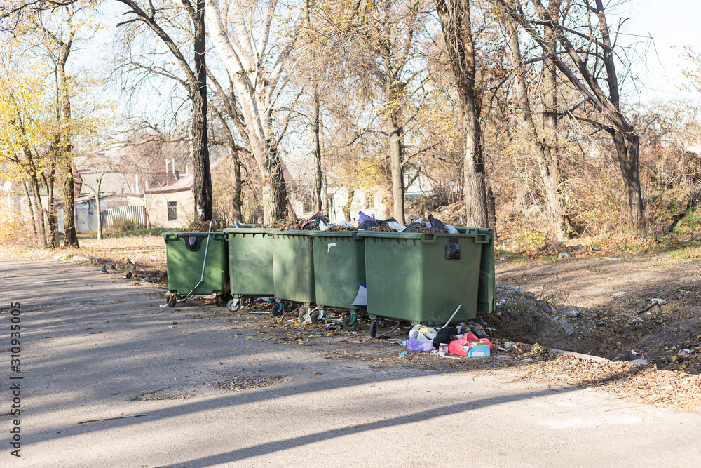 Overfilled garbage cans stand in the middle of the street. Trash spills out, polluting the environment and harming the environment. Overfilled garbage cans stand in the middle of the street. Trash spills out, polluting the environment and harming the environment.