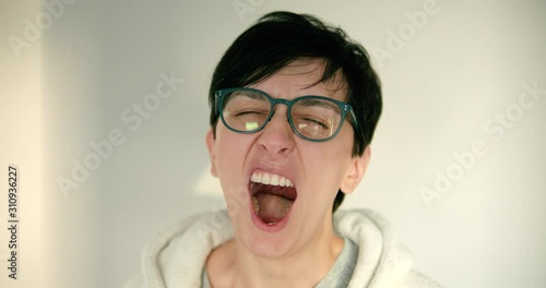 Close up of young woman with glasses and short hair yawning in slow motion