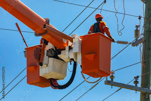 A man wearing high visibilty personal protective equipment, PPE, is seen working on high voltage overhead power cables and a utility pole at height photo