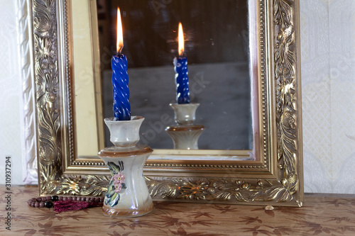 Fortune telling with a candle and a mirror. In the candlestick there is a burning candle, next to the rosary. The candle is reflected in the mirror.