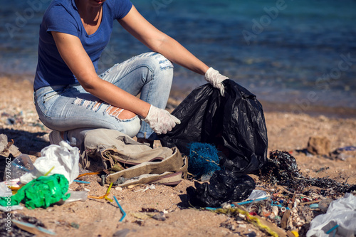 Woman with black bag collect garbage on the beach. Environmental pollution concept