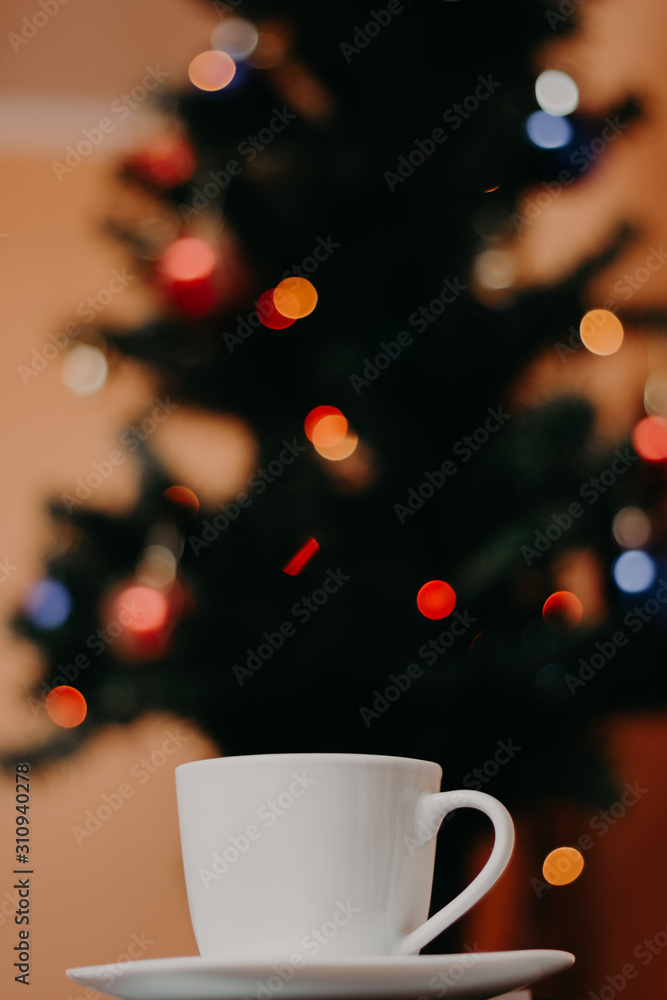 Obraz premium White color cup of coffee with Christmas tree in the background