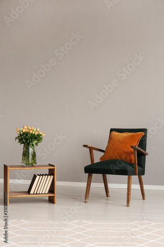 Green retro armchair in grey living room interior with wooden furniture