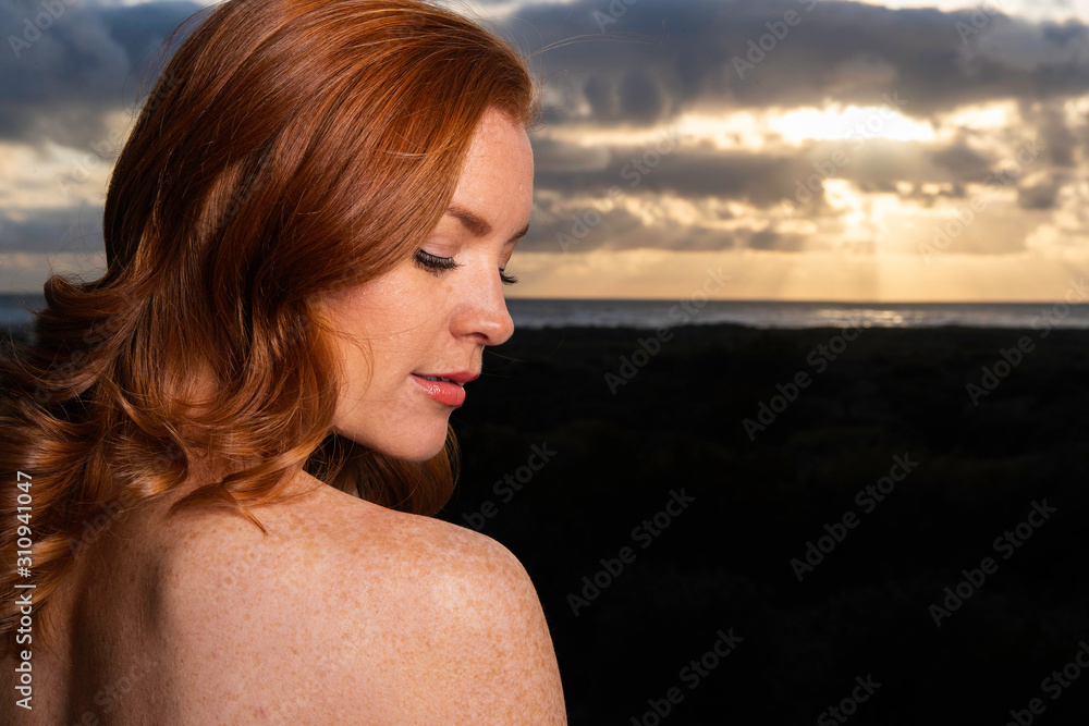 Beautiful woman with red hair looks over her shoulder during sunset at the beach Beautiful woman with red hair looks over her shoulder during sunset at the beach